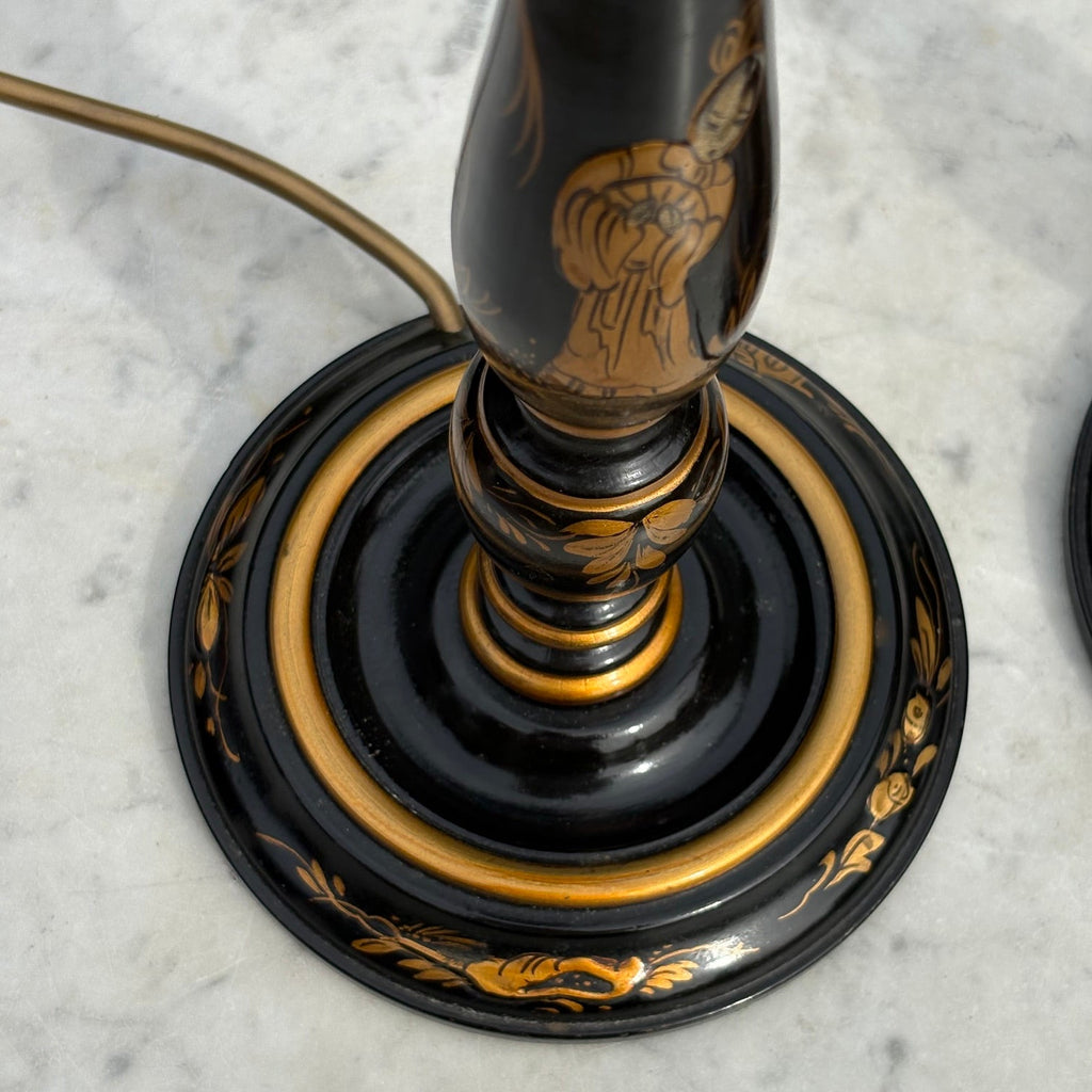 Close-up of a black and gold decorative lamp base with ornate gold floral scrollwork on a light marble surface.