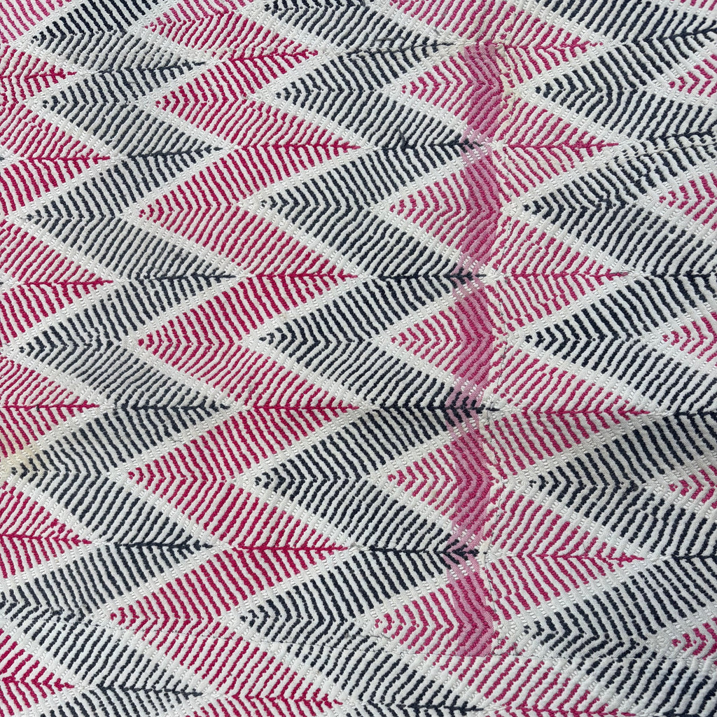A close-up of an antique woven textile with a repeating chevron pattern in pink, black, and white, featuring a partial pink border along the bottom edge.