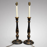 A pair of antique chinoiserie black and gold candlestick-style table lamps with white candle sleeves, shown against a neutral gray background.
