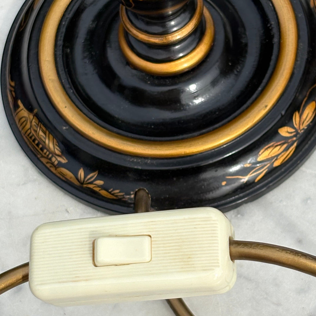 Close-up of an antique chinoiserie table lamp base with a glossy black and gold lacquered finish, featuring a cream-colored plastic switch on the cord.