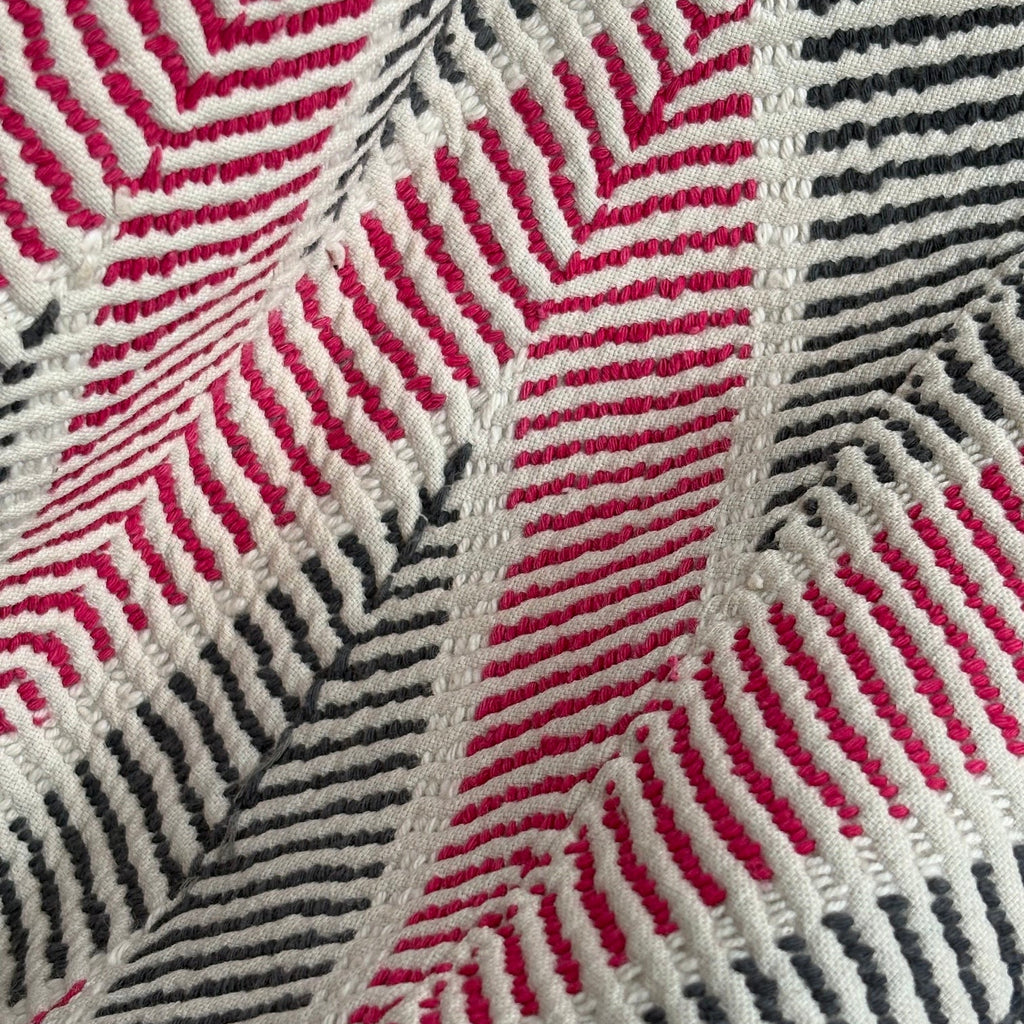 Close-up of a woven antique textile with a geometric herringbone pattern in bright pink, off-white, and dark gray.